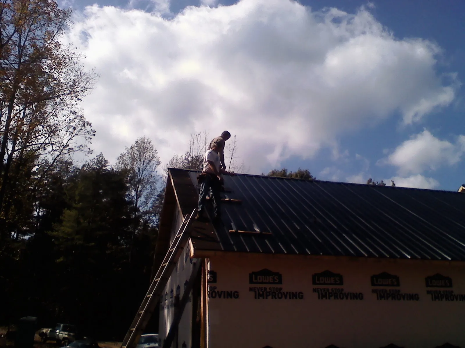 Roofer fastening dark metal panels high against a cloudy sky, from a Roof Inspection job in Easton
